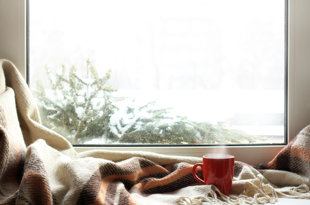 stock photo of a white upvc window with red mug of tea, a blanket, and snow on a christmas tree outside - Ace Double Glazing