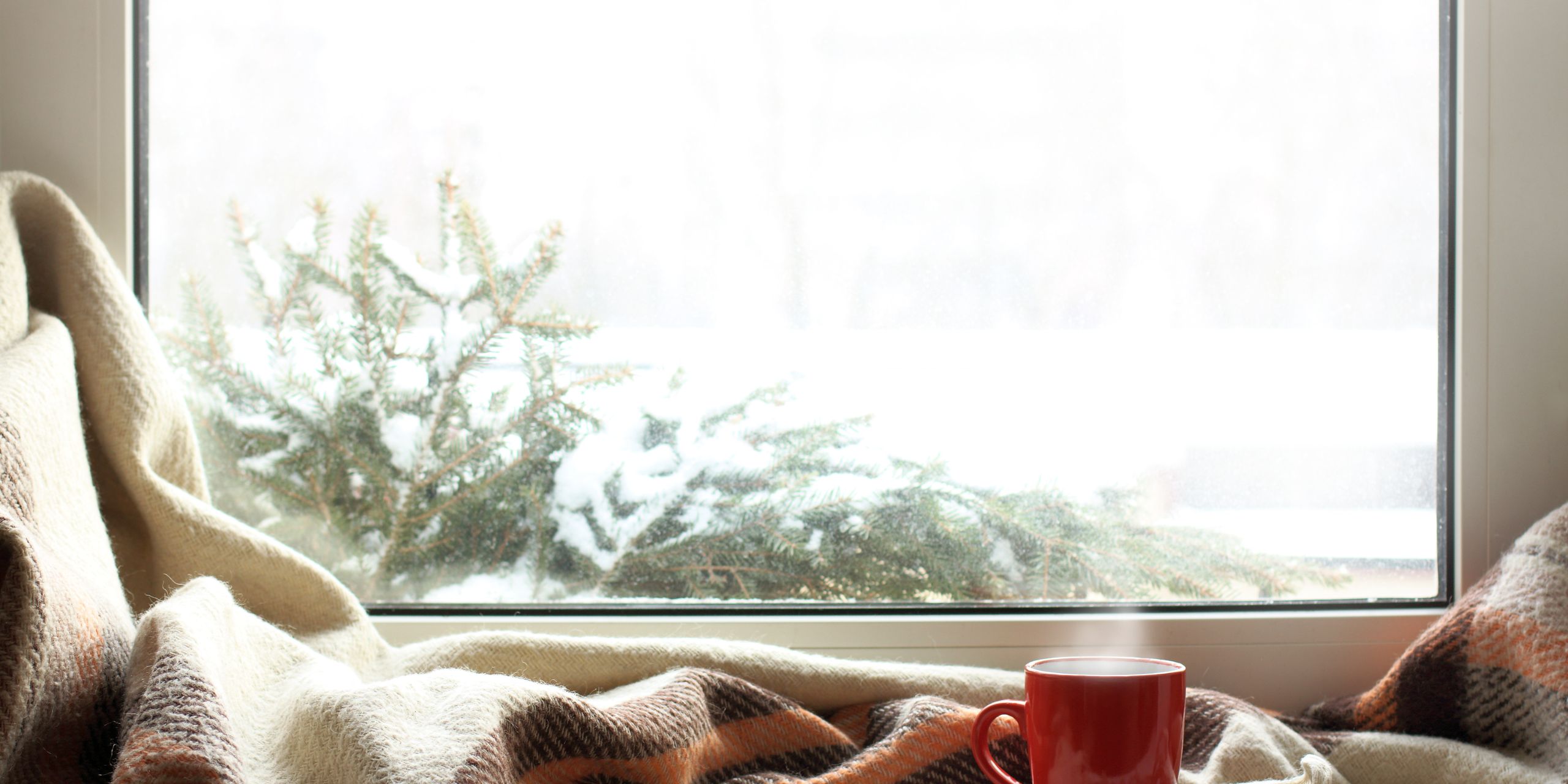 stock photo of a white upvc window with red mug of tea, a blanket, and snow on a christmas tree outside - Ace Double Glazing
